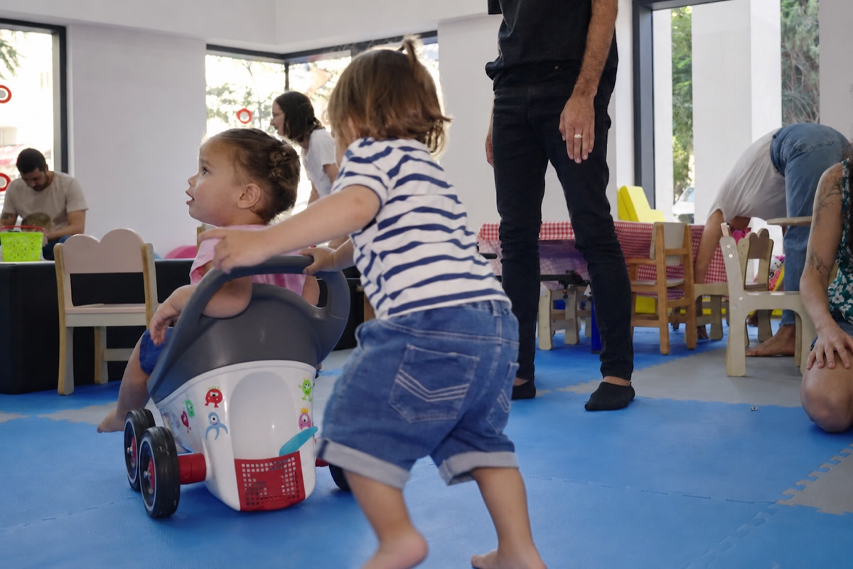 פעוט דוחף פעוטה בעגלת משחק במשחקייה של המרכז הגאה