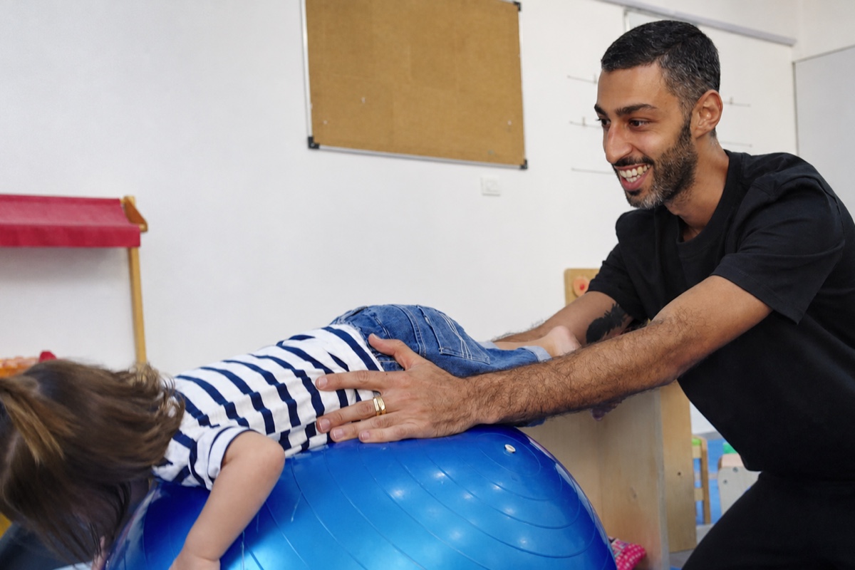 מבוגר משחק עם פעוטה על כדור פיזיו במשחקייה של המרכז הגאה